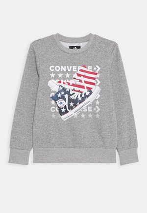 Sweatshirt gris arborant un graphique de baskets Converse rayées rouges et blanches avec un motif d'étoiles bleues, accompagné du texte "Converse" en caractères gras.