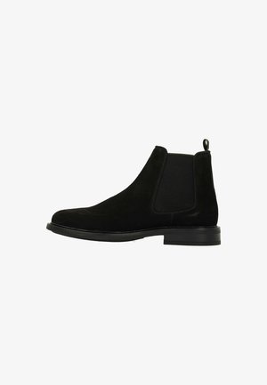 Black suede Chelsea boots with elastic side panels, rounded toe, and a pull tab on the heel. Flat rubber sole, minimalist design.