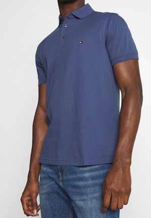 Mann trägt ein navyblaues Polohemd mit kurzen Ärmeln und kleinem Logo auf der Brust, kombiniert mit mittelblauen Jeans.