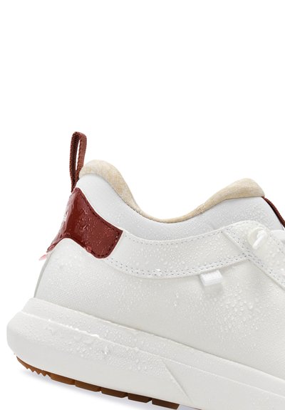 Bílé tenisky s texturovaným povrchem, hnědými akcenty na patě, smyčkou na tahání a kapkami vody na materiálu.