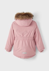 Giacca isolante rosa con cappuccio, dotata di rifinitura in pelliccia sintetica. Vita regolata, polsini elasticizzati e un accento riflettente sulla schiena.