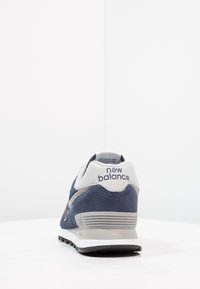 Mörkblå mockaskor med grå accenter, vit sula och "New Balance"-logotyp på hälen. Rundad design med vadderad krage.