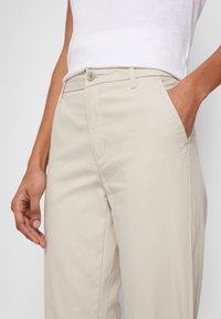 Pantalon en coton beige clair à coupe droite, doté de poches latérales et d'une taille boutonnée pour une fermeture sécurisée.