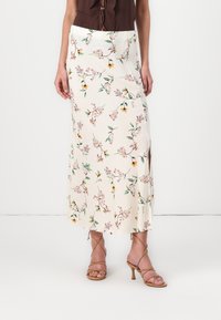 Blomstrete midiskjørt i kremfarge med rosa og gule blomster; glatt stoff, sideslitt, kombinert med brune, strappy høyhæler.