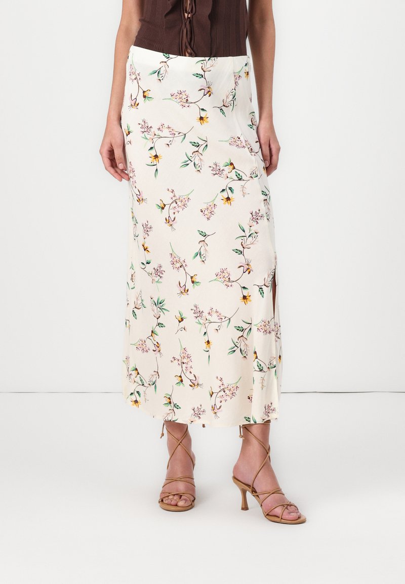 Blomstrete midiskjørt i kremfarge med rosa og gule blomster; glatt stoff, sideslitt, kombinert med brune, strappy høyhæler.
