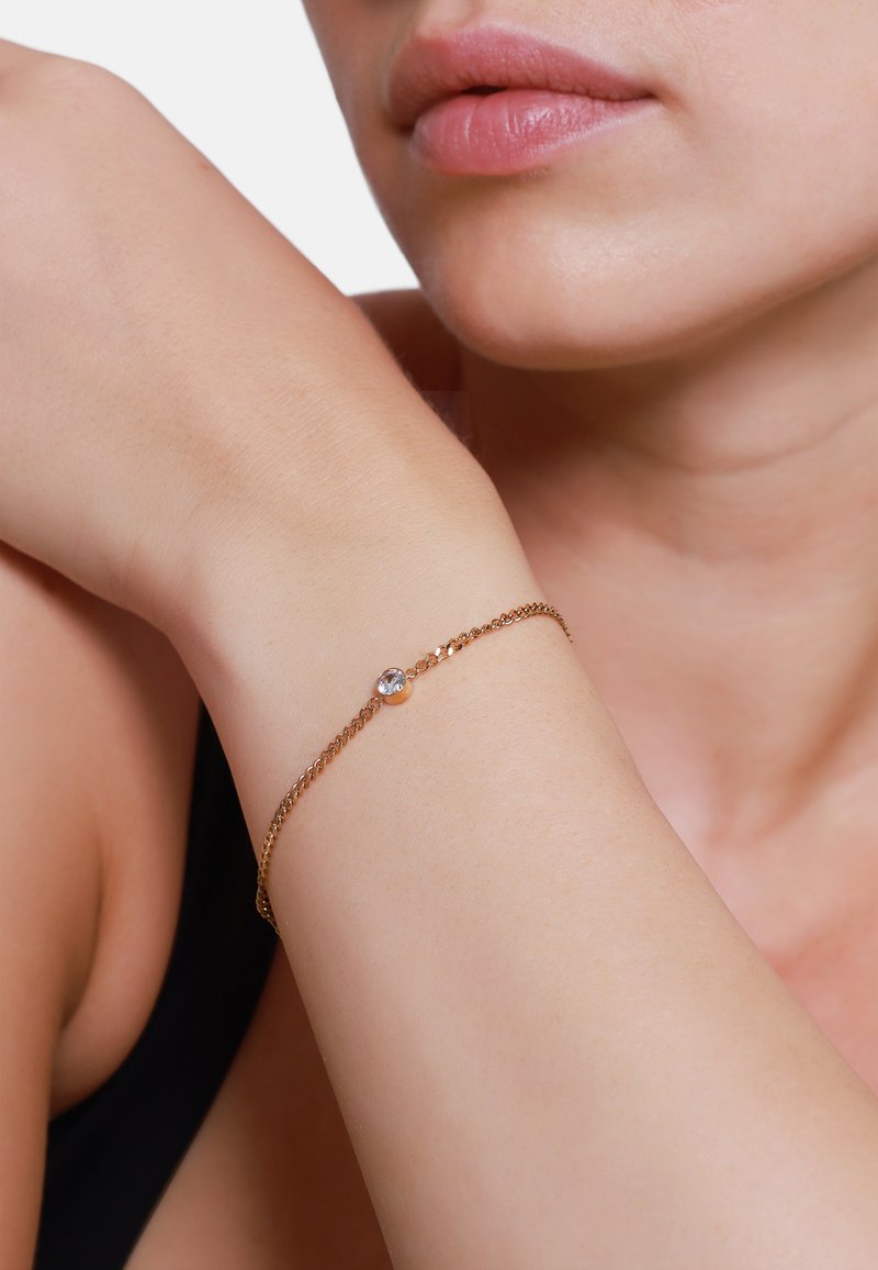 Bracciale a catena tono oro con un singolo brillante trasparente, link delicati e un design minimalista su un polso nudo.