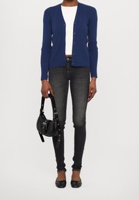 Blå stickad kofta med v-ringning och knäppning, bärs över en vit topp, matchat med mörkgrå skinny jeans och svarta ballerinas.