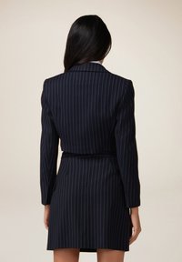 Abito blazer a righe navy con maniche lunghe, vita con cintura e rever; design strutturato con texture liscia.