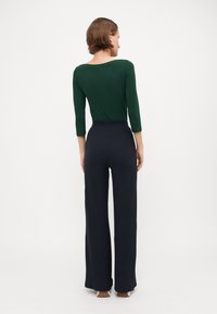 Haut à manches longues vert associé à un pantalon large taille haute de couleur sombre. Texture côtelée sur le pantalon, tissu lisse sur le haut.