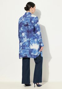 Maglietta lunga blu con effetto tie-dye, colletto con bottoni, orlo leggermente curvato e maniche lunghe, abbinata a pantaloni in denim scuri a zampa d'elefante e tacchi.