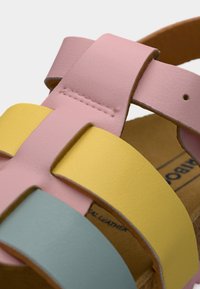 Δερμάτινα σανδάλια με ροζ, κίτρινες και μπλε λουριά πλεγμένα μαζί. Το εσωτερικό έχει ταμπά φινίρισμα με ορατές ραφές.