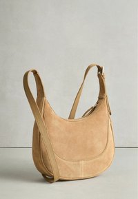 Barna velúr válltáska ívelt kialakítással, széles pánttal és cipzáras záródással. Texturált felület minimális díszítéssel.