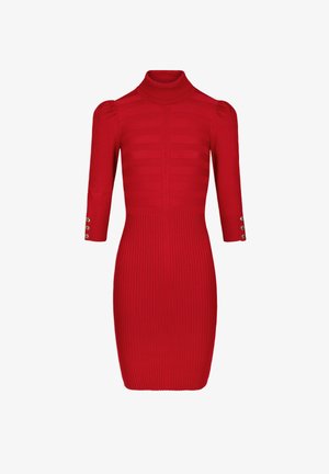 Czerwona sukienka z prążkowanego materiału, z wysokim dekoltem, rękawami do trzech czwartych i guzikami przy mankietach. Posiada dopasowaną górę i rozkloszowany dół.