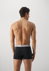 Boxers atléticos negros con cinturilla de marca blanca, diseño ajustado, textura suave y corte a mitad del muslo. Modelo mostrado de espaldas.