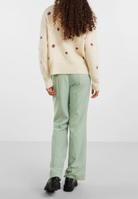 Krämfärgad tröja med röd blommig broderi, matchad med mintgröna byxor och svarta platåskor. Texturen verkar mjuk och bekväm.