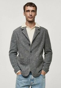 Gray wool blend jacket with a tailored fit, notched lapels, two front pockets, and a single button closure over a white collared shirt.