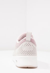 Nike tenisky s horní částí z prodyšné síťoviny v světle růžové barvě, s texturovanou šedou semišovou patou a bílou polstrovanou podrážkou s logem na zadní straně.