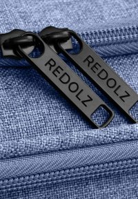 Zwei schwarze Reißverschluss-Zipper mit der Aufschrift "REDOLZ" an einem teilweise geschlossenen blauen gewebten Reißverschluss.