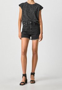 Musta farkkushortsit repsottavilla lahkeensuilla, yhdistetty tummanharmaaseen, valkoisilla pisteillä koristeltuun hihattomaan paitaan ja mustiin korkokengän sandaaleihin, joissa on niittejä.