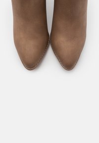 Brune ankelstøvler i imiteret læder med spids tå og kontrastsyning, med en glat tekstur og et tætsiddende design.