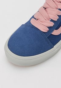 Baskets en daim bleu avec des lacets roses et un détail latéral rose, avec une semelle en caoutchouc blanche et vue rapprochée de la pointe de la chaussure.