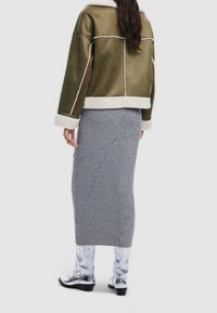 Olivgrön mockajacka med vita fårskinnsdetaljer, kombinerad med en grå ribbad kjol och glansiga vita cowboyboots med präglad yta.