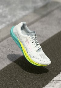 Chaussure de course légère avec un dessus en mesh blanc respirant, une semelle teal et jaune, et un accent rose ; dotée d'un système de laçage.