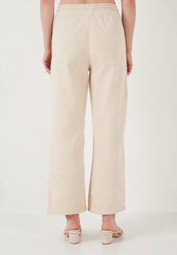 Beige wide-leg pants made of soft cotton fabric, featuring an elastic waistband and no visible pockets, with a smooth textured finish.