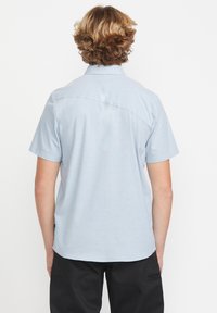 Chemise à manches courtes en bleu clair, avec une couture de yoke au dos, un col et une coupe décontractée. Fabriquée à partir d'un tissu léger avec une texture lisse.