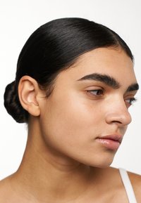 Profilo di una persona con capelli scuri e lisci raccolti in un elegante chignon, pelle chiara, zigomi pronunciati, labbra piene e trucco naturale.