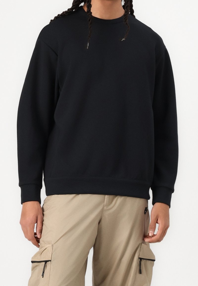 Černá mikina s kulatým výstřihem, vyrobená z měkké látky; má dlouhé rukávy a volný střih, doplněná cargo kalhotami.