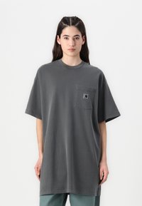 T-shirt over-sized in cotone grigio con collo rotondo, maniche corte e una tasca sul petto sinistro con patch del logo. Tessuto morbido, vestibilità casual.