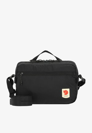 Saco de nylon preto com uma pega superior, correia ajustável, bolso frontal com fecho e um pequeno logótipo com uma raposa vermelha no canto inferior direito.