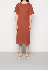 Rustfarbendes gestricktes Kleid mit kurzen Ärmeln, runder Halslinie und vertikalen Texturdetails, getragen mit hellen Plateausandalen.