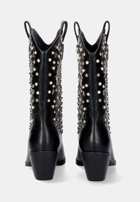 Botas de cuero negro hasta el tobillo con punta en forma de pico, presentan remaches metálicos y acentos de estrella en el costado. Tacón cuadrado y lengüetas para ponérselas fácilmente.