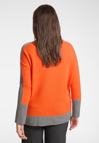 Oranger und grauer Pullover mit gerippter Textur. Verfügt über abfallende Schultern und ein Color-Blocking-Design mit einem auffälligen grauen Streifen am unteren Saum.