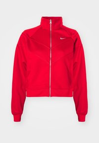 Röd Nike zip-up jacka med hög krage, ribbat mönster och chevron-design på framsidan. Har en silverfärgad logotyp på övre vänstra sidan.