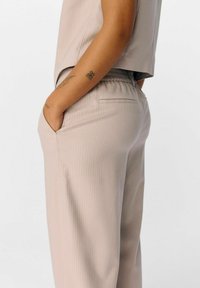 Helle beige, gestreifte Stoffhosen mit elastischem Bund und seitlichen Taschen, die eine lockere Passform und eine glatte Textur aufweisen.