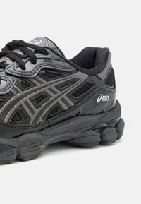 Černé a šedé běžecké boty ASICS s prodyšnou tkaninou a syntetickými překryvy, černými tkaničkami, polstrovanou podrážkou a logem na boku, zobrazené na bílém pozadí.