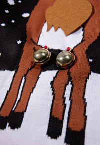 Pull en tricot avec fond noir et motif de renne marron et blanc. Des clochettes dorées avec des accents rouges y sont attachées.