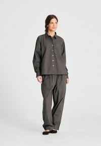 Camicia button-up grigia scura, dalla vestibilità ampia, con taschino sul petto, abbinata a pantaloni larghi coordinati. Il tessuto sembra leggero e testurizzato.