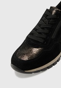 Mustad sneaker, millepuudega ja metallikrebitud nahkdetailidega. Omab musti paelu, tekstureeritud tallat ja madalat profiili.