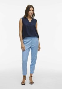 Top sans manches bleu marine avec un décolleté en V, associé à un pantalon ajusté bleu clair et des sandales noires à lanières. Tissu lisse, coupe slim.
