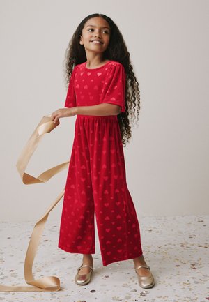Rød jumpsuit med hjerteprint, korte pufærmer, elastisk talje og brede ben. Guld ballet flats fuldender outfittet.
