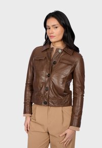 Veste en cuir marron avec un col, boutons sur le devant, quatre poches et taille ajustée ; assortie à un pantalon beige taille haute.
