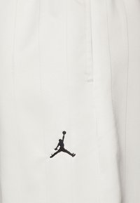 Logo en silhouette noire d’un joueur de basket sautant avec un ballon sur un tissu blanc avec des rayures verticales subtiles.
