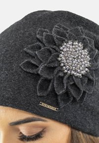 Cappello grigio lavorato a maglia con un'applicazione floreale testurizzata e dettagli in perle sul lato; presenta un’etichetta con logo in metallo sul bordo.