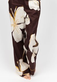 Bruine wijde broek met grote ivoorkleurige bloemenpatronen en gele accenten, vervaardigd uit een gladde, lichtgewichte stof.