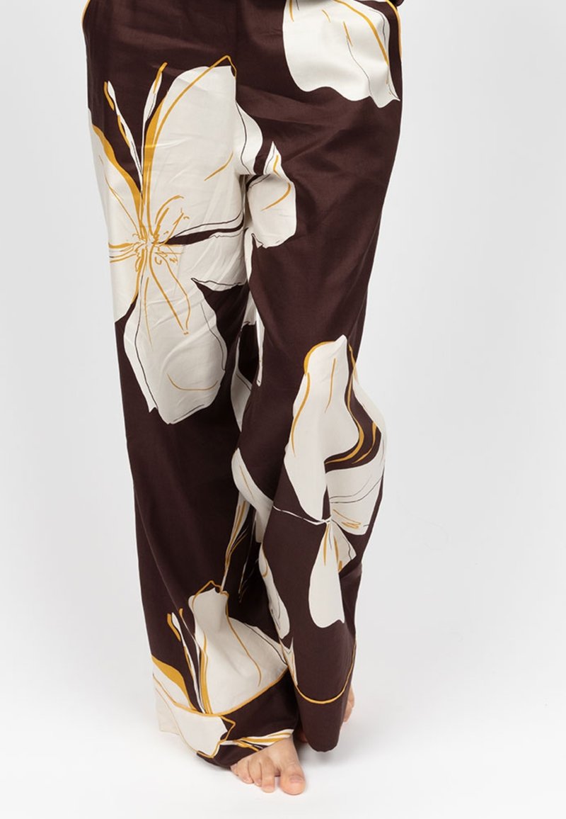 Bruine wijde broek met grote ivoorkleurige bloemenpatronen en gele accenten, vervaardigd uit een gladde, lichtgewichte stof.