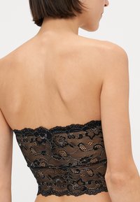 Crna čipkasta bralette, bez naramenica, cvjetni uzorak, prozirna tekstura, valoviti rubovi, prilagođeni silueta bez vidljivih detalja.